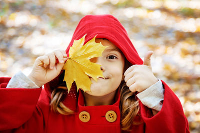 Girl with thumbs up holding leaf during autumn