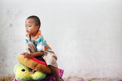 Portrait of cute baby boy sitting against wall