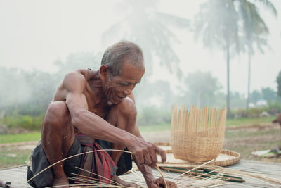 Shirtless senior man making straw basket