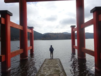 Rear view of boy standing on jetty against lake