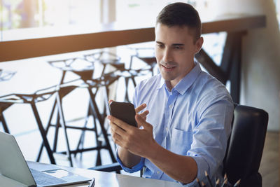 Young man using mobile phone while sitting on table