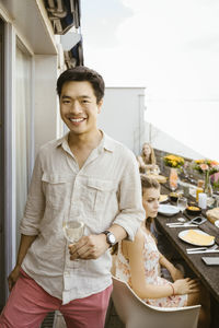 Portrait of smiling man holding wineglass while standing in balcony