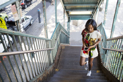 High angle view of woman using phone while moving up on steps