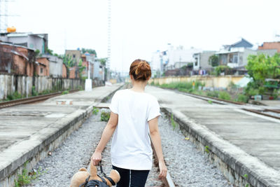 Rear view of holding teddy bear while walking on railroad track