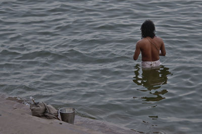 Rear view of shirtless man sitting in water