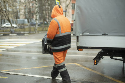 Worker puts cargo in transport. orange clothes for work. cleaning road. man throws bag.