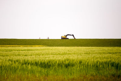 Excavator on grassy field against clear sky