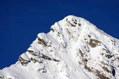 Low angle view of snowcapped mountains against clear blue sky