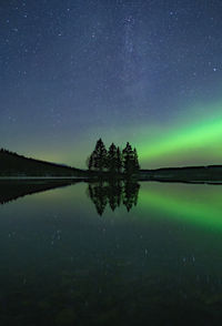 Starfield with aurora borealis reflections in a still lake with small island in the center