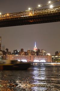 Illuminated bridge over river by buildings in city at night