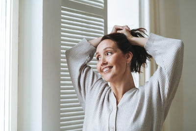 Young beautiful woman forty year with brunette hair in cozy knitted cardigan near window at home