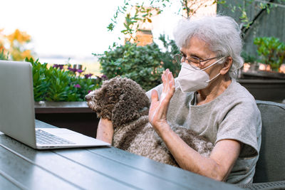 Old woman wearing face mask and her dog chatting via internet