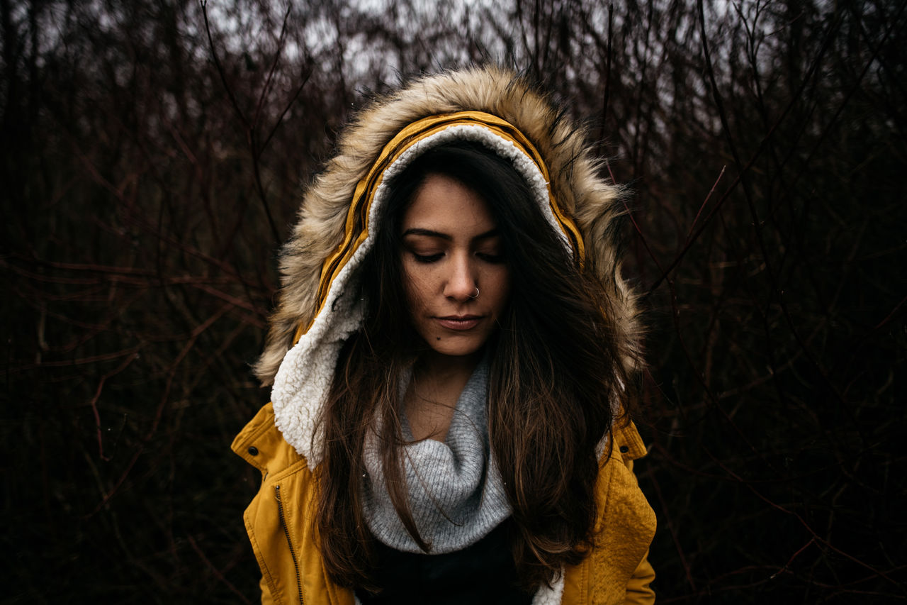 front view, one person, clothing, real people, young women, lifestyles, portrait, young adult, tree, warm clothing, winter, jacket, headshot, standing, leisure activity, hair, fur, looking down, contemplation, hood - clothing, outdoors, hairstyle, scarf, beautiful woman