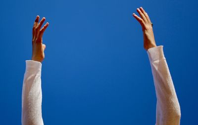 Midsection of man with arms raised against blue sky