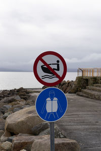 Close-up of road sign by sea against sky