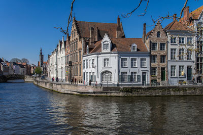 View of buildings by river against blue sky