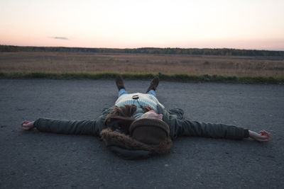 Man lying on land against sky during sunset