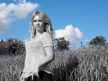 Portrait of smiling young woman standing on field against sky