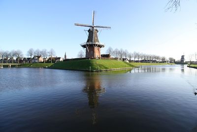 Traditional windmill by lake against sky