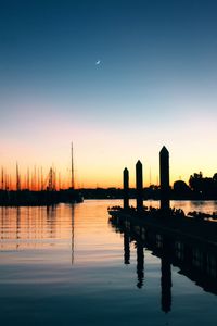 Silhouette of wooden posts in lake against sky during sunset