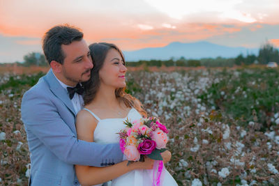 Smiling bride and groom with bouquet romancing on field