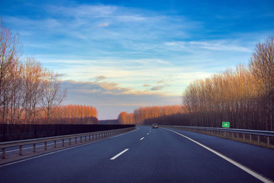 Road by trees against sky during sunset