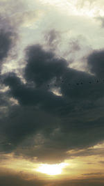 Low angle view of silhouette birds flying against dramatic sky