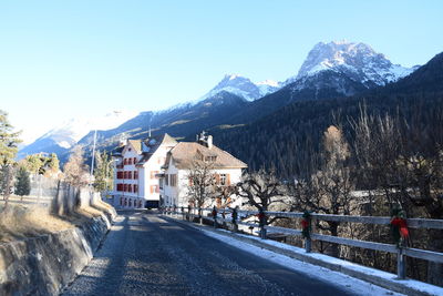 Road by snowcapped mountains against clear blue sky