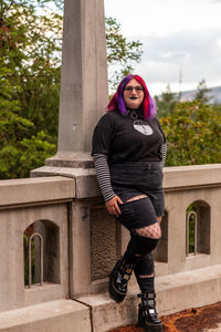 Low angle view of young woman standing against railing of bridge