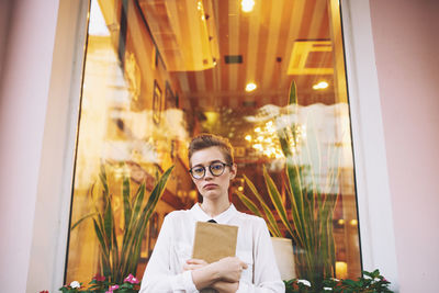 Portrait of young woman standing against window