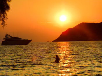 Silhouette man in sea against orange sky