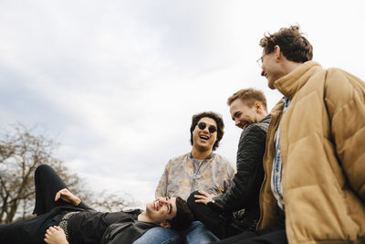 Cheerful male friends spending leisure time against sky