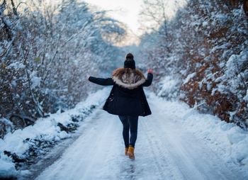 Rear view of happy woman walking on snow covered road during winter