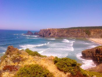 Scenic view of sea and cliff against clear blue sky