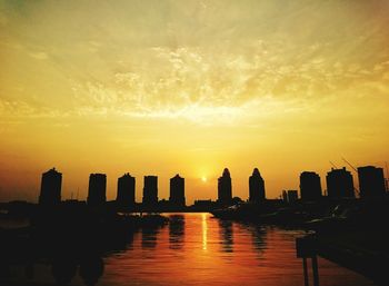 Silhouette city by sea against sky during sunset