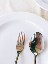 Close-up of fork by spoon in plate on table