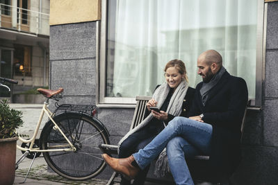 Mid adult business people using smart phone on bench against building