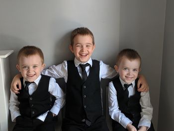 Portrait of smiling brothers wearing suits against wall at home