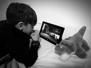 Boy using digital tablet by stuffed toy on bed at home