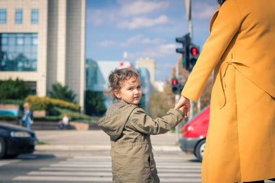 Midsection of mother holding hand of daughter on road in city