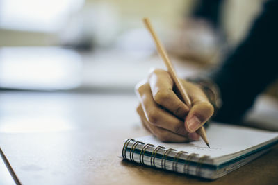 Cropped hand of female student writing on notepad on desk