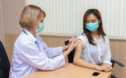 Doctor wearing mask vaccinating patient in hospital