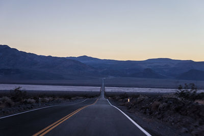 Road leading towards mountains against clear sky