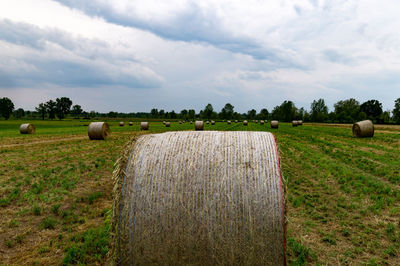 Hay bales on field against cloudy sky