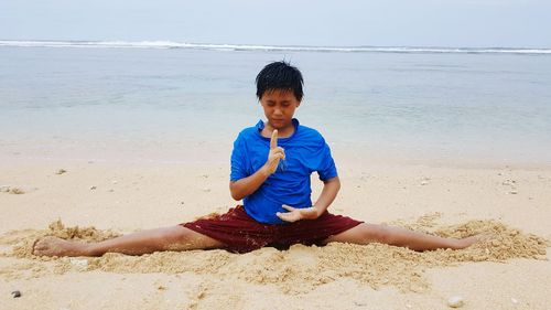 Boy doing the splits on beach against sky