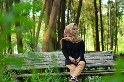 Thoughtful woman wearing hijab looking away while sitting in forest