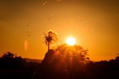 Silhouette person holding sun during sunset