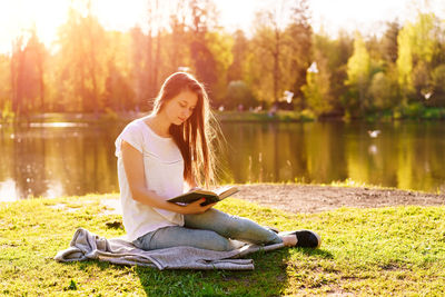 Young hipster girl enjoys sun and nice warm day reading book while relaxing