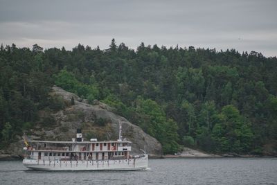 Boat on river by trees against sky