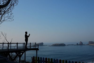 Silhouette man standing by sea against clear sky during sunset or sunrise.